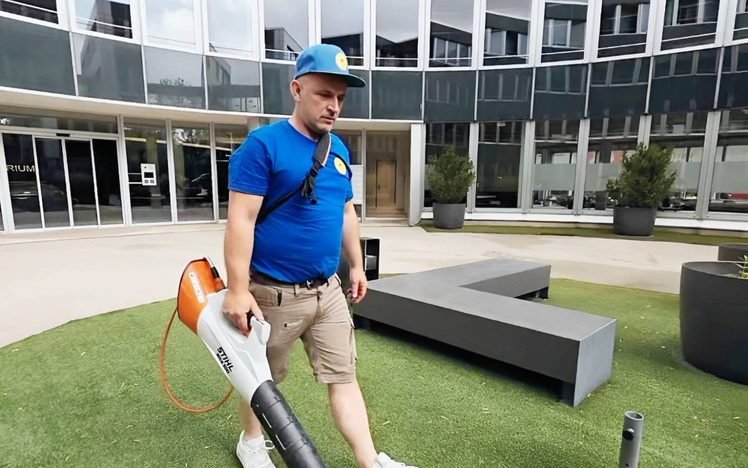 Mitarbeiter beim Laubblasen im begrünten Innenhof des Rundbaus